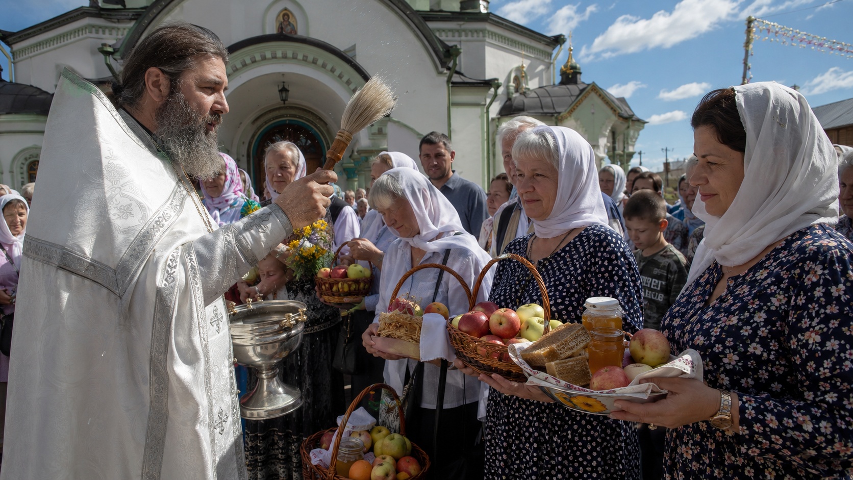Священник освящает мёд и яблоки у церкви в августовский день